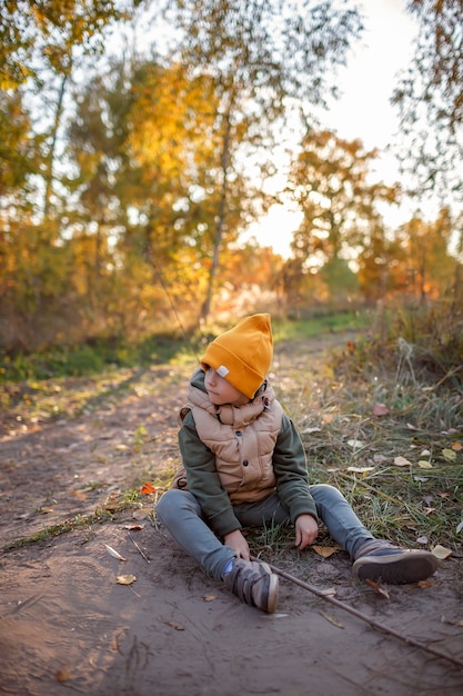 Boy with wooden stick walks through the path and explores forest during autumn walk