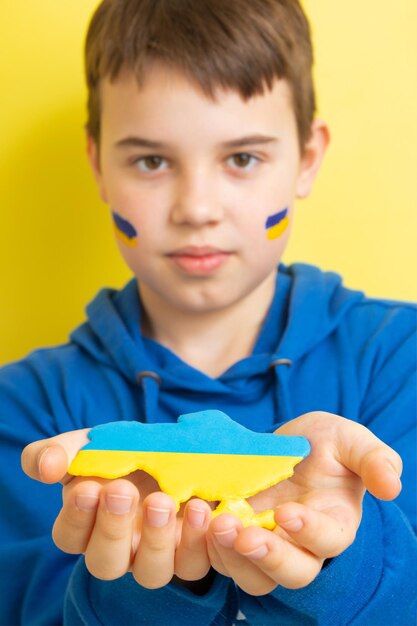 A boy with a yellow and blue flag on his cheeks holds a map of Ukraine in national colors