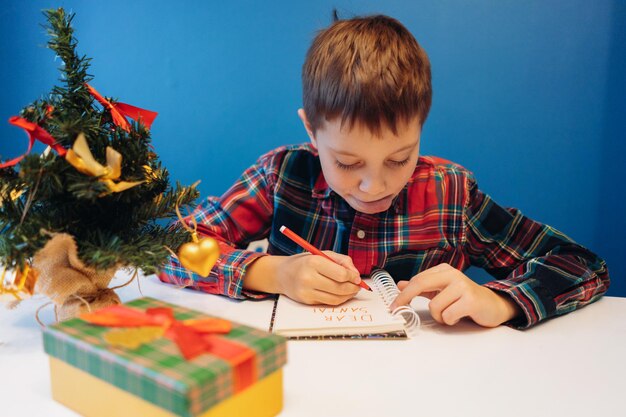 Photo boy writing letter for santa claus for christmas sitting at the table at home