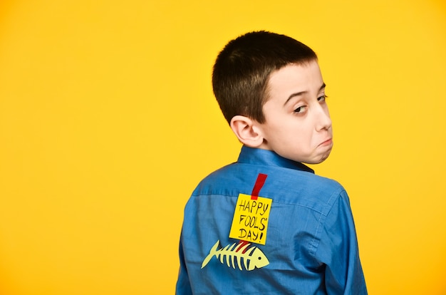 The boy on a yellow background in a blue shirt with a fish glued tape and a piece of paper on his back