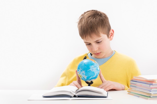 Boy in yellow jumper does geography lessons Schoolboy sits at table and carefully studies the globe