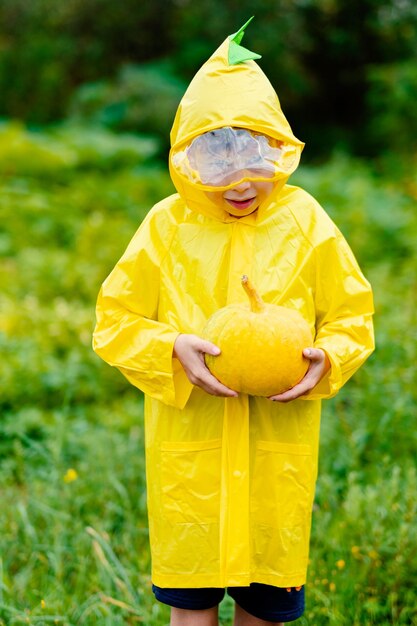 Foto ragazzo con un impermeabile giallo tiene una zucca gialla che si prepara per il raccolto di zucca di halloween