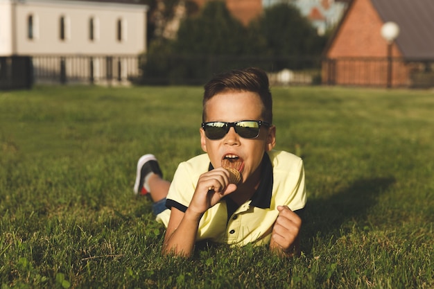 Boy in a yellow T-shirt sits on the grass with ice cream.