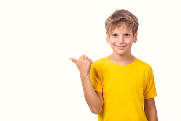 Boy in yellow Tshirt isolated on white background points his thumb to side and smiles Copyspace