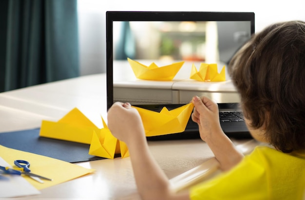 a boy in a yellow Tshirt at an online origami workshop a paper boat