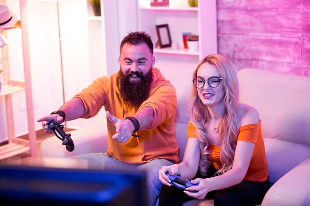 Photo boyfriend cheering her beautiul girlfriend while she's playing online games using wireless controller. room with neon light.