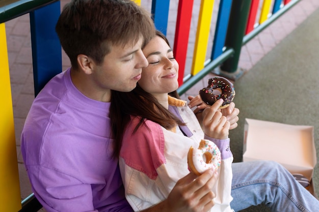 Photo boyfriend and girlfriend eating donuts outdoors