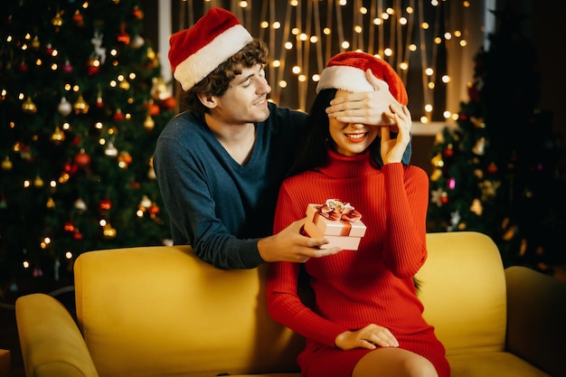 Парень делает рождественский подарок своей девушке. Молодая пара празднует дома. Мужчина удивляет женщину.