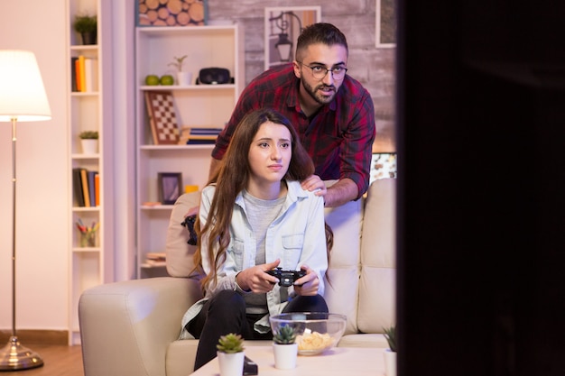 Фото Парень помогает своей девушке выиграть в видеоиграх. девушка играет в видеоигры по телевидению с помощью контроллеров.