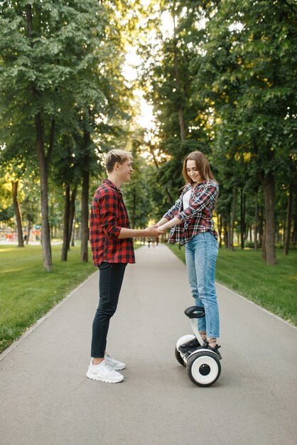 Boyfriend teaches his girl to ride on gyro board in summer park.