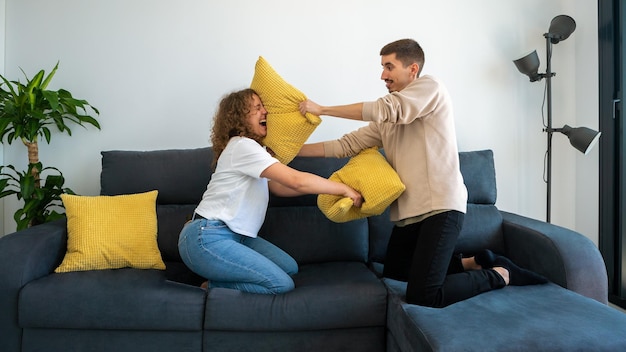 Boyfriends having fun playing together on sofa at home fighting with cushion