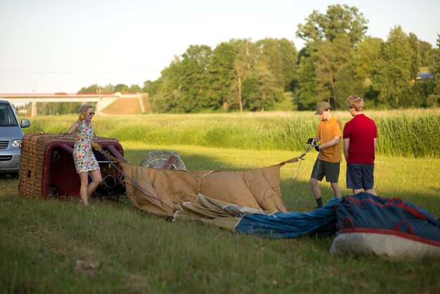 写真 夕暮れの空に向かって草原で熱気球を準備するパイロットを助ける少年たち