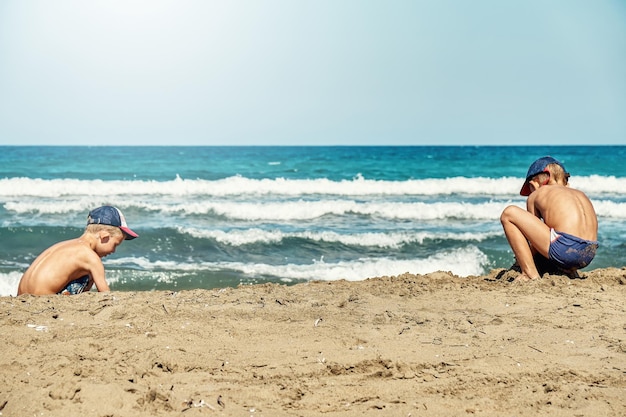 Boys build sand castle on surf line against azure sea waves rolling with heavy foam on Prasonisi