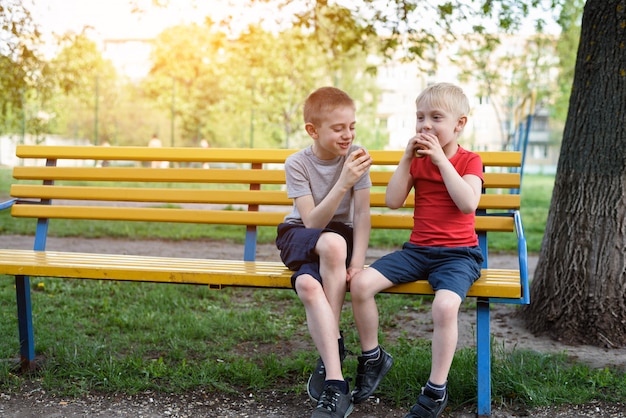 boys having a snack on a bench in the park and chat