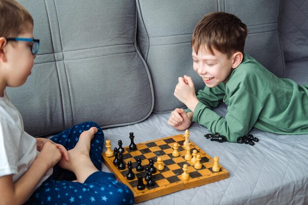 Boys play wooden chess lying on a gray sofa