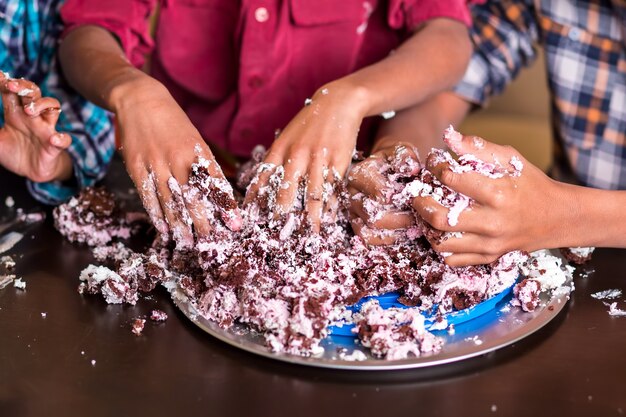 手でケーキを壊す男の子。 3人の子供の手がケーキを壊します。これで終わりです。私たちはできる限りのことをしました。