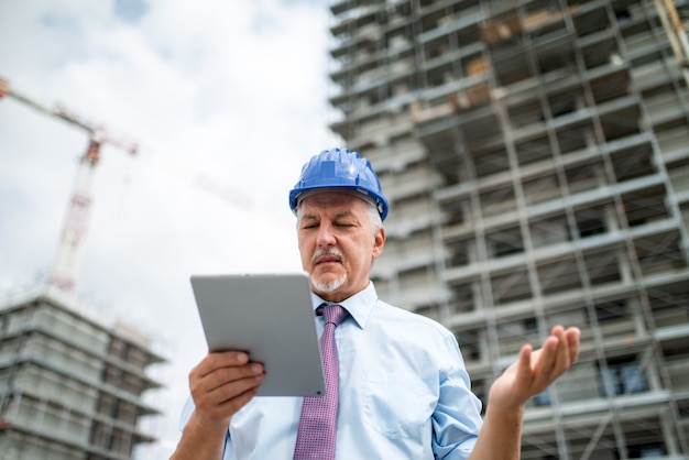 Boze architect die zijn tablet voor een bouwwerf gebruikt