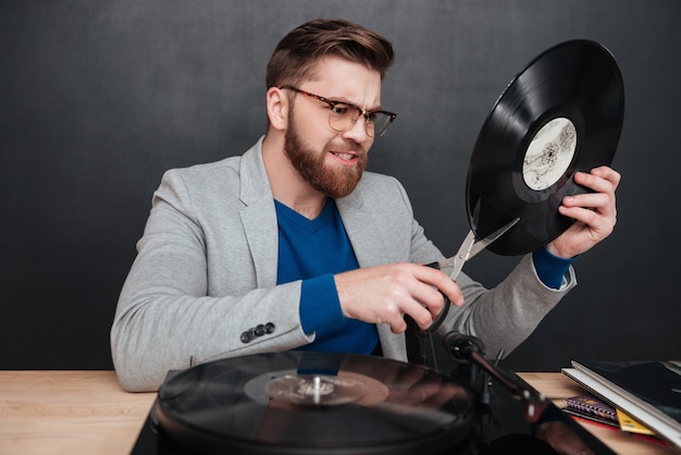 Boze bebaarde jonge man in glazen snijden vinyl record met een schaar