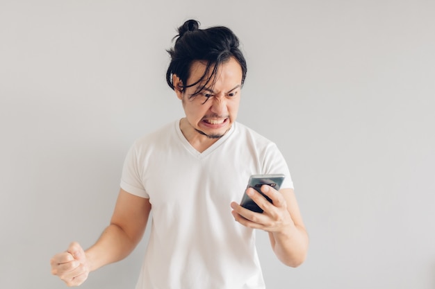 Boze en woedende man met lange haren in witte t-shirt gebruikt smartphone