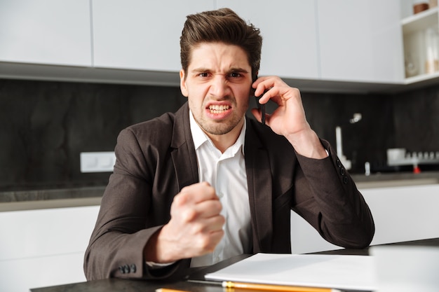 Boze jonge zakenman die door mobiele telefoon spreekt.