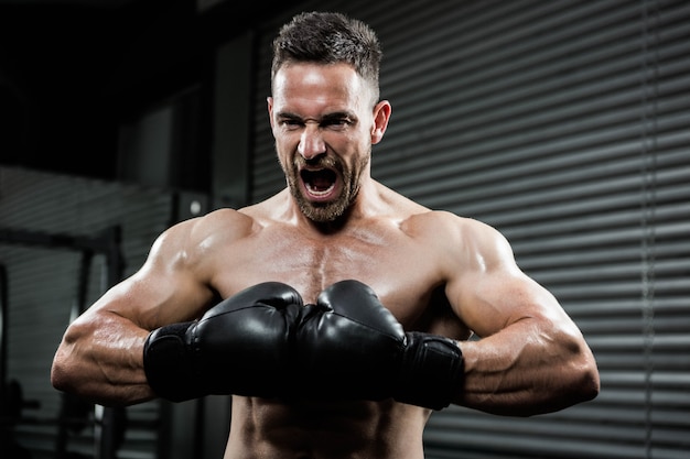 Boze shirtless mens die met bokshandschoenen bij de crossfitgymnastiek schreeuwt