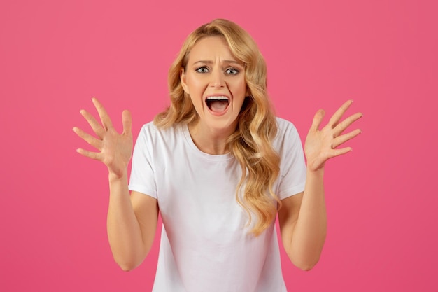 Boze, verdrietige jonge blonde vrouw schreeuwt op een roze achtergrond.