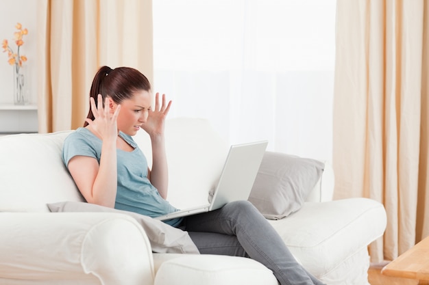 Boze vrouw die met haar computer gokt terwijl het zitten op een bank