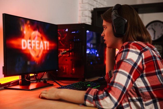 Boze vrouw gamer zittend aan tafel, online spelen op een computer binnenshuis