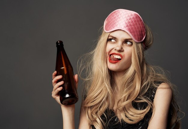 Foto boze vrouw met een flesje bier in haar hand met lichte make-up en een roze slaapmasker foto van hoge kwaliteit