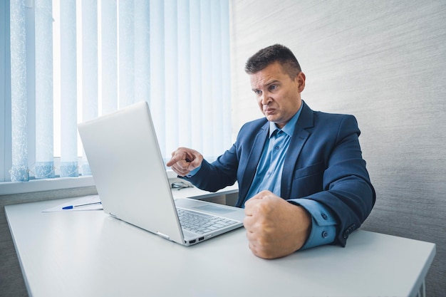 Boze zakenman in een jas slaat zijn vuist op tafel in woede internet of computer werkt niet slecht nieuws faillissement