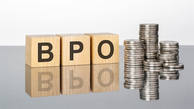 Bpo text on wooden cubes on a cold grey light background with stacks coins