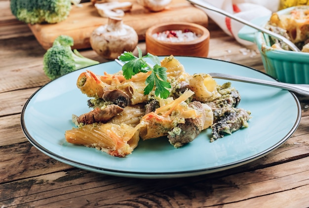 Braadpan met pasta, champignons, broccolisaus en kaas op een rustieke houten achtergrond