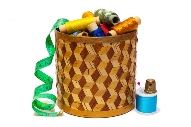 Photo braided manually birchbark box with spools of colored threads and dressmakers measuring tape