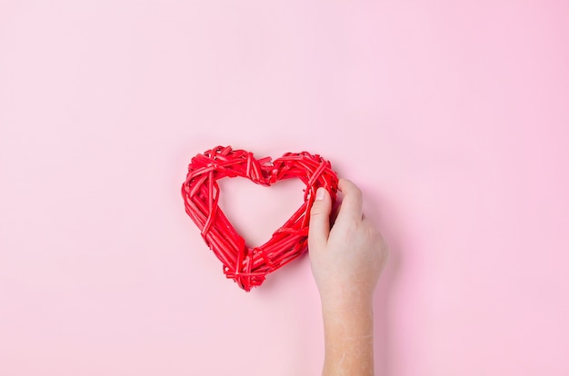 Braided wicker red  heart of twigs in the hands of a girl on pink background.