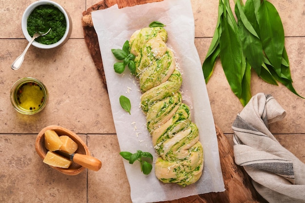 Braided wild garlic pesto brioche homemade raw or uncooked\
fresh pull apart bread with wild garlic pesto on wooden board on\
old beige tiles background italian bread copy space top view