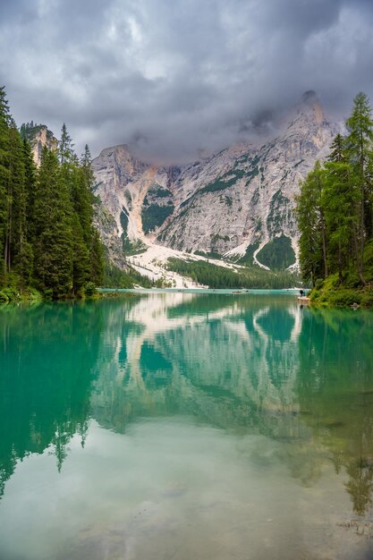 Photo braies lake surrounded by pine forests and the rocky ranges of the dolomites in cloudy day italy