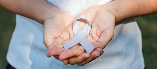 Brain cancer awareness month, woman hand holding grey color\
ribbon for supporting people living. healthcare and world cancer\
day concept