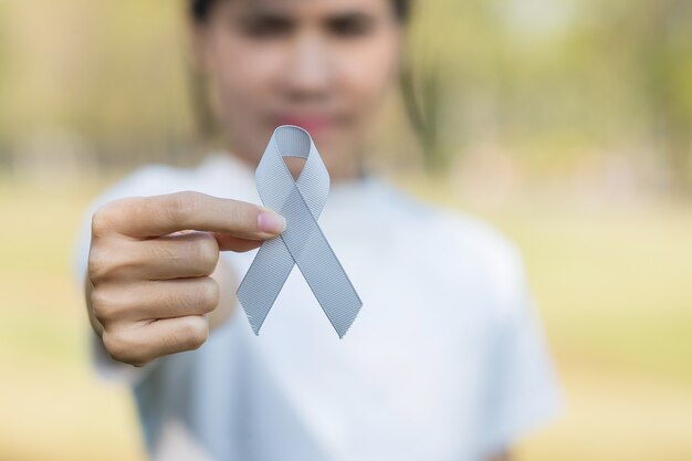 Mese di consapevolezza del cancro al cervello, mano della donna che tiene il nastro di colore grigio per sostenere le persone che vivono.