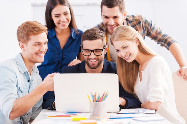 Brainstorm. Groep vrolijke zakenmensen in slimme vrijetijdskleding die samen naar de laptop kijken en glimlachen