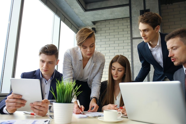 Brainstorm. Group of business people looking at the laptop together. One business woman looking at camera