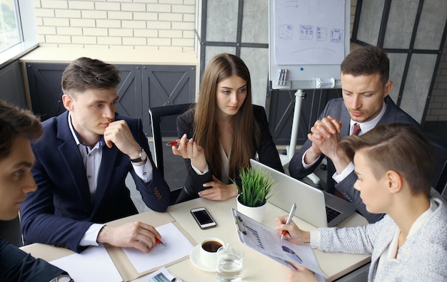 Brainstorm. Group of business people looking at the laptop together. One business woman looking at camera