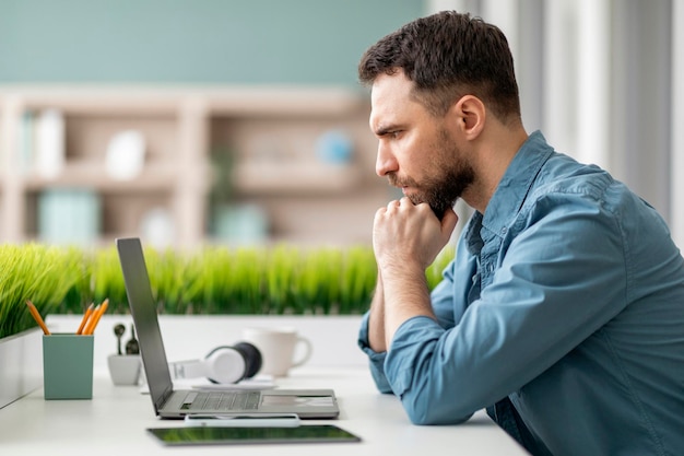 Brainstorming concept pensive man sitting at desk and looking at laptop screen