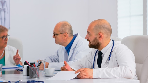 Brainstorming teamwork of physicians solving problems of patients in modern hospital meeting room having medical conference. Team of doctors talking about symptoms of disease in clinic office.