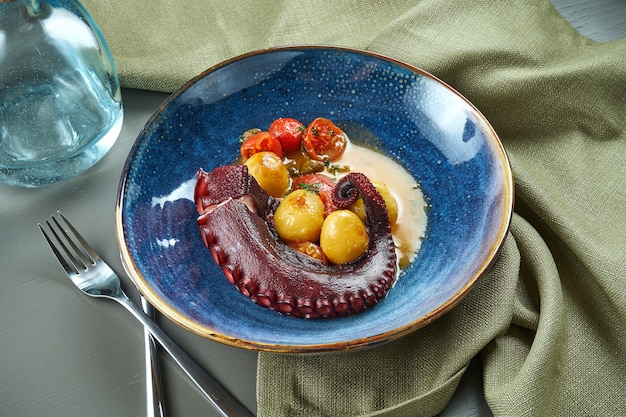 Braised octopus tentacle with tomatoes in a creamy sauce in blue bowl on wooden table. Delicious and luxury seafood