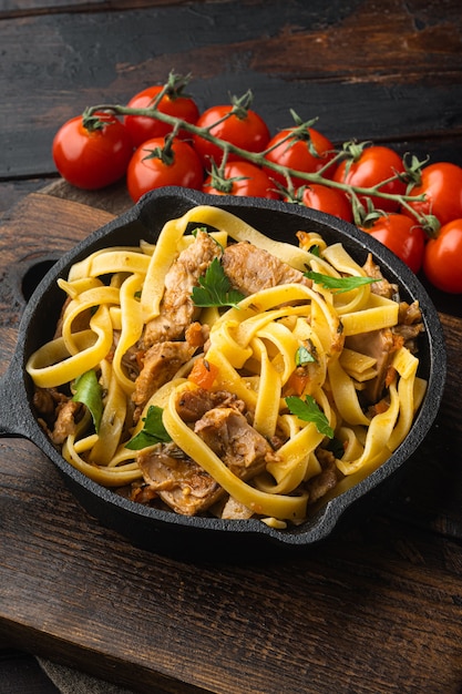 Coniglio brasato con rosmarino, aglio e tagliatelle di pasta o set di pappardelle, in padella o pentola di ghisa, sul vecchio tavolo di legno scuro