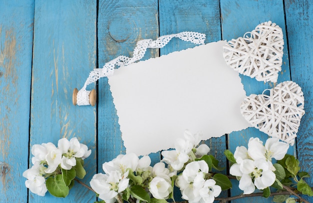 Photo a branch of a blossoming apple tree, two hearts, a lace ribbon and an empty sheet of paper