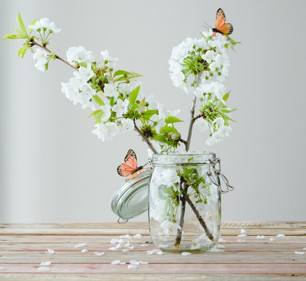 Branch of cherry blossom with butterflies in glass jar on wooden