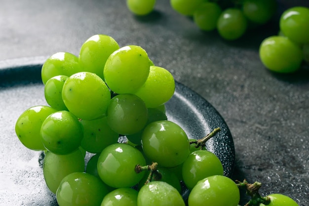 A branch of green juicy grapes in a plate with copy space Black background Front view Place for writing Suitable for Summer