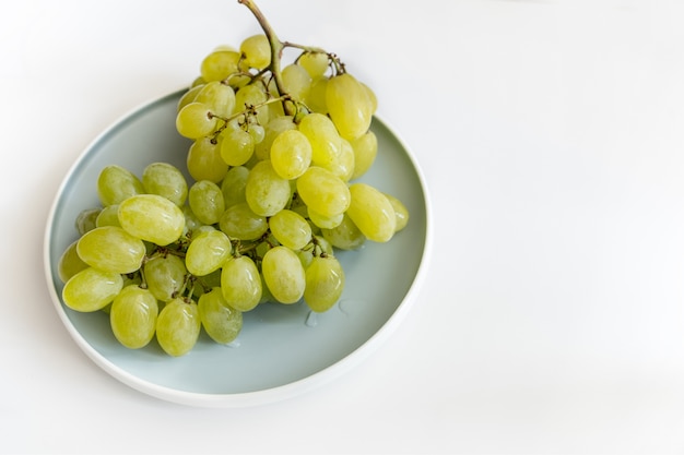 a branch of green sweet grapes lies on a plate