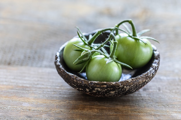 Branch of green tomato in a ceramic cup on a wooden table